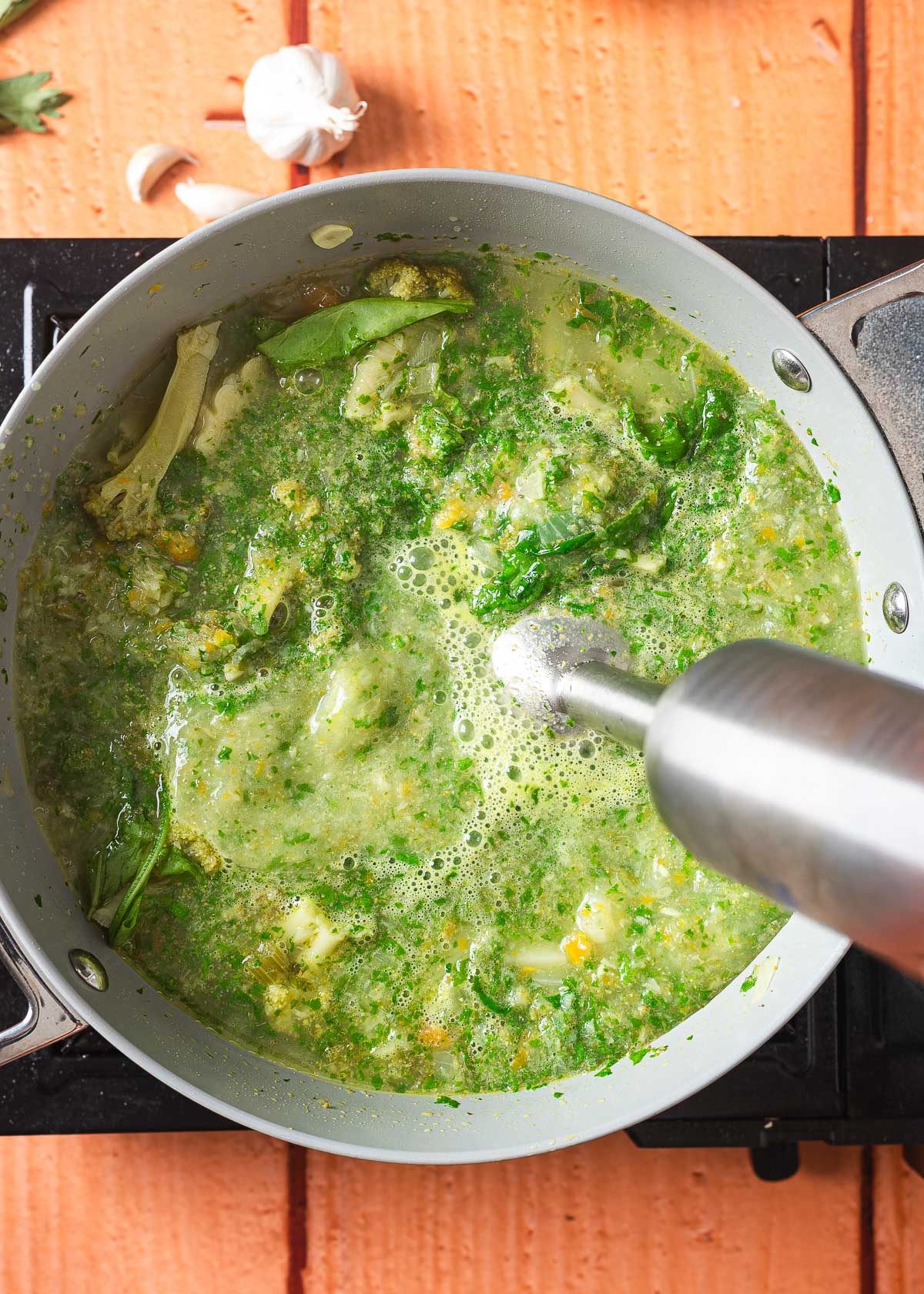 An immersion blender starting the blending process on vegan broccoli soup.