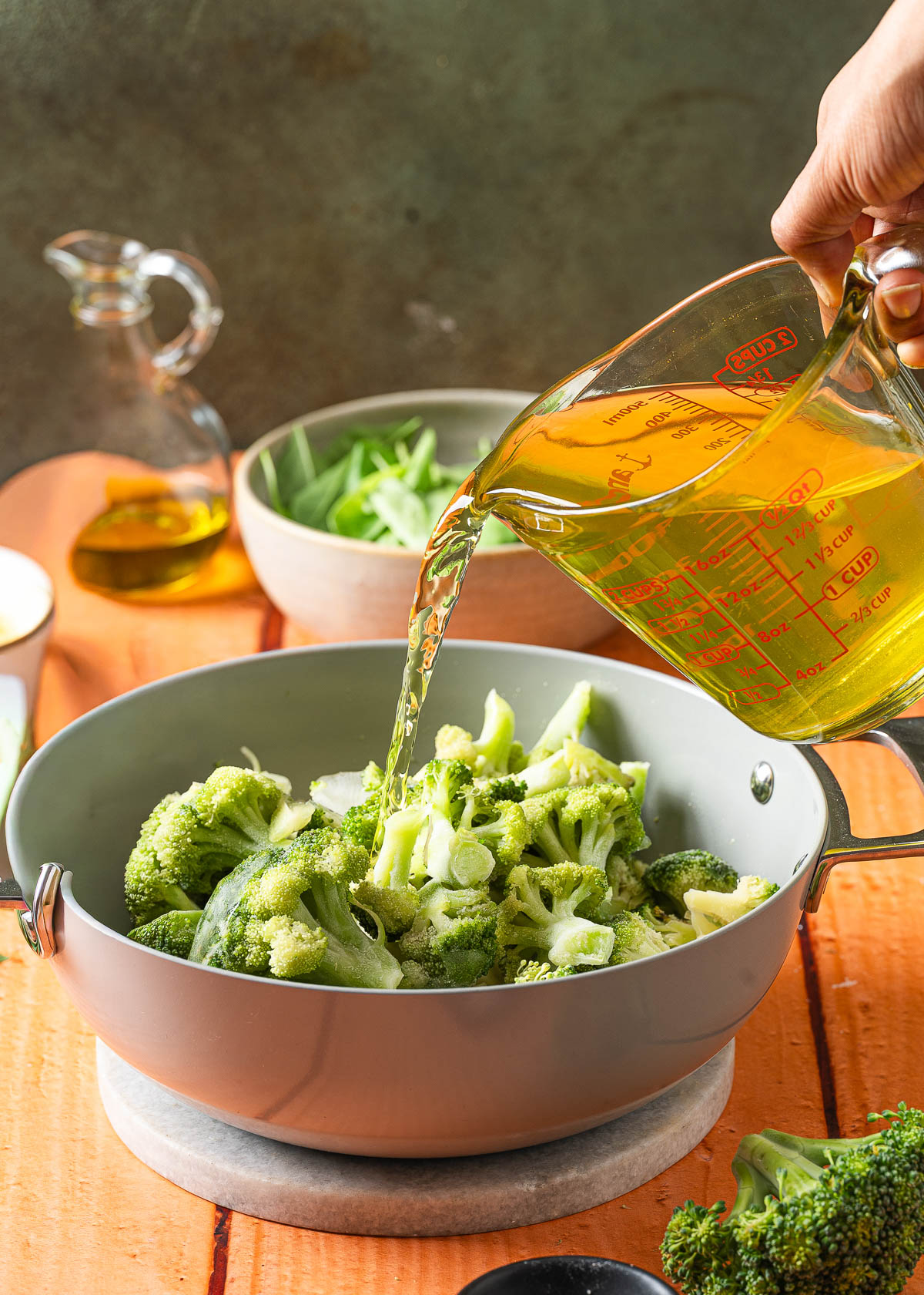 A hand pouring vegetable broth into a pot filled with broccoli florets.