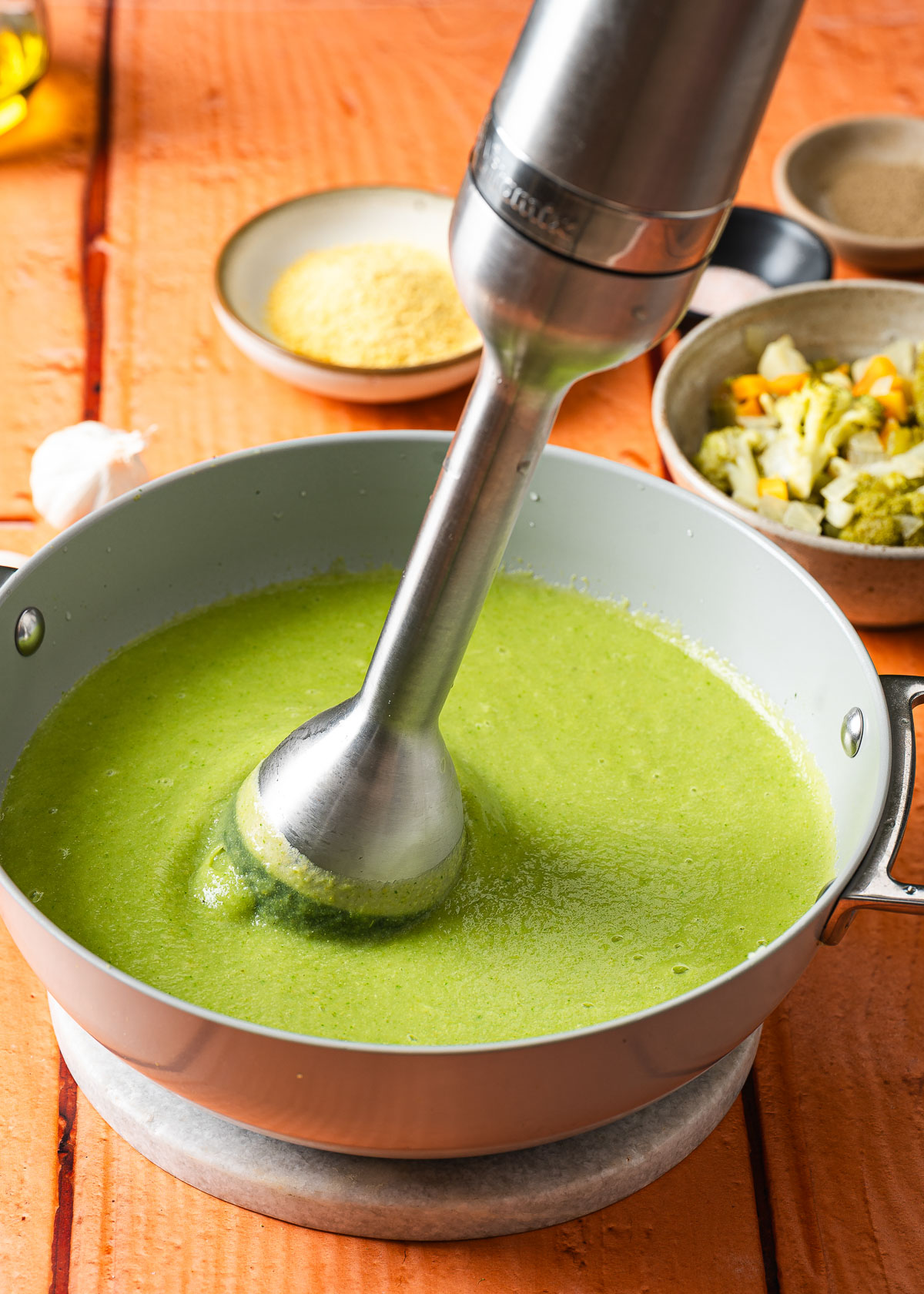 An image showcasing an immersion blender blending vegan broccoli soup to the right consistency.