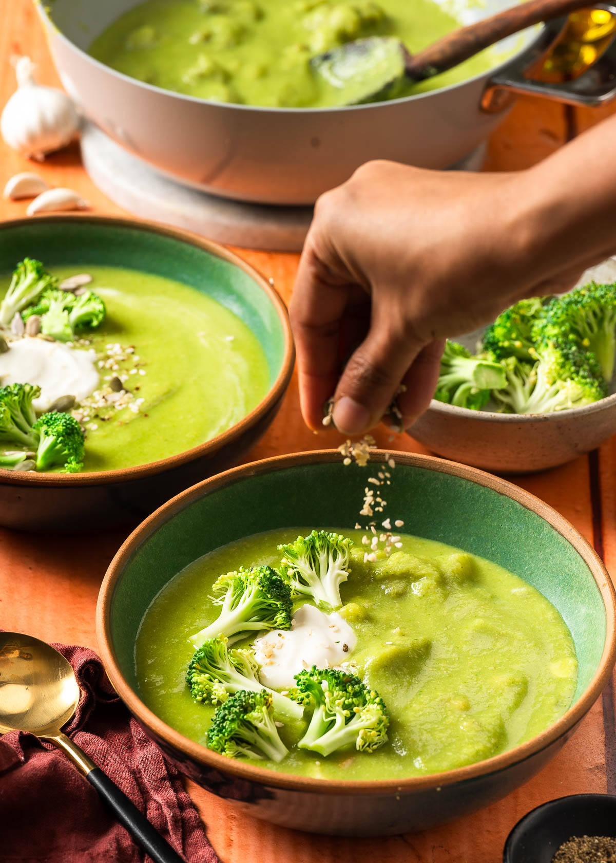 A hand adding toppings to ready-to-eat bowls of soup.