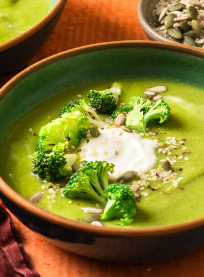 A detailed shot of creamy vegan broccoli soup topped with dairy-free sour cream, fresh broccoli, and sesame seeds.