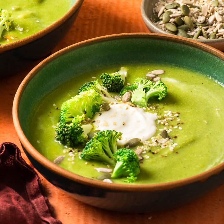 A detailed shot of creamy vegan broccoli soup topped with dairy-free sour cream, fresh broccoli, and sesame seeds.