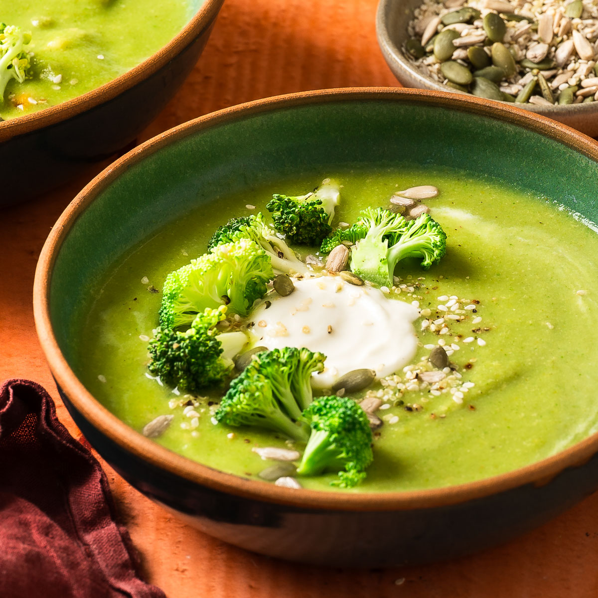A detailed shot of creamy vegan broccoli soup topped with dairy-free sour cream, fresh broccoli, and sesame seeds.