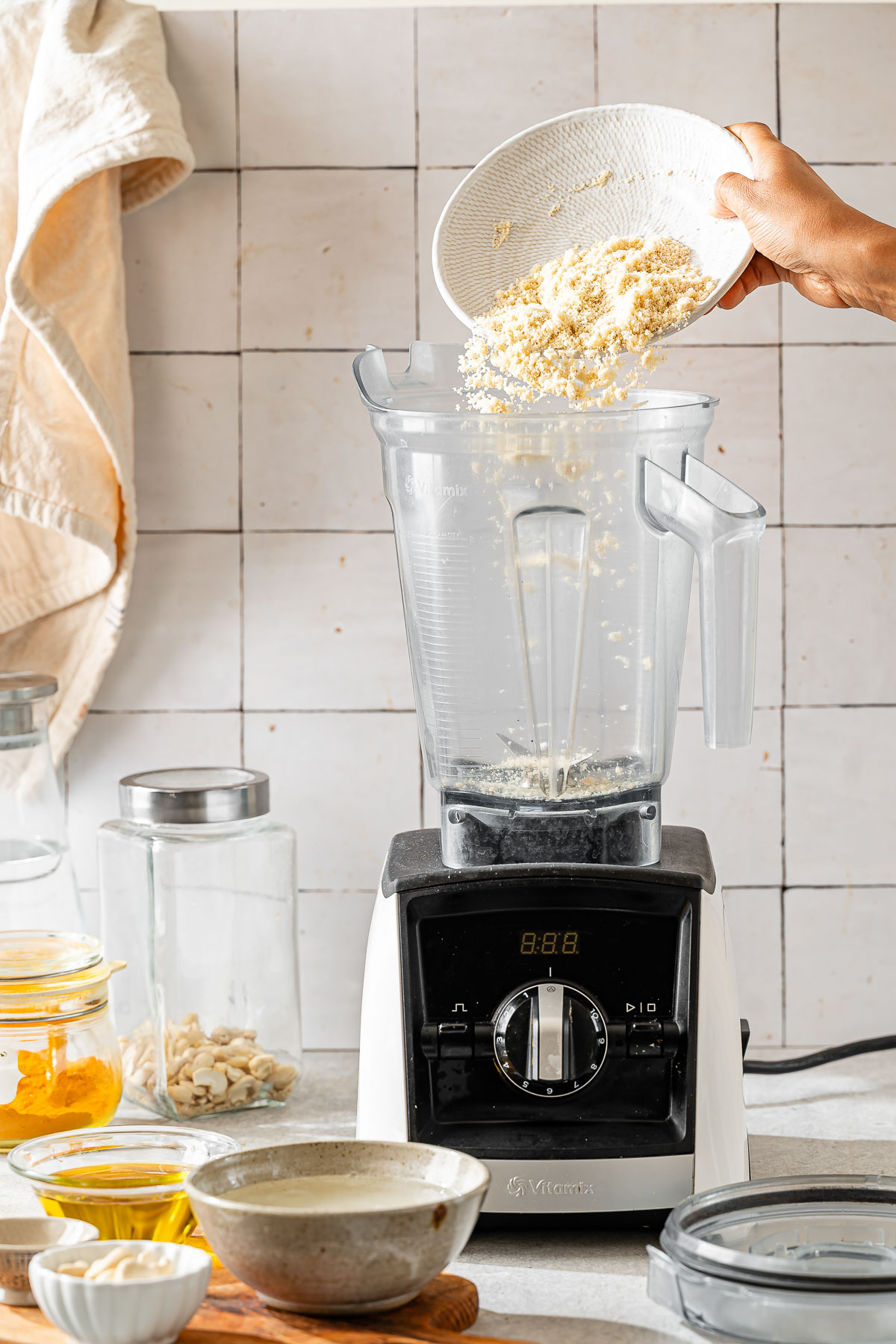 A person adding almond flour in a high-speed blender