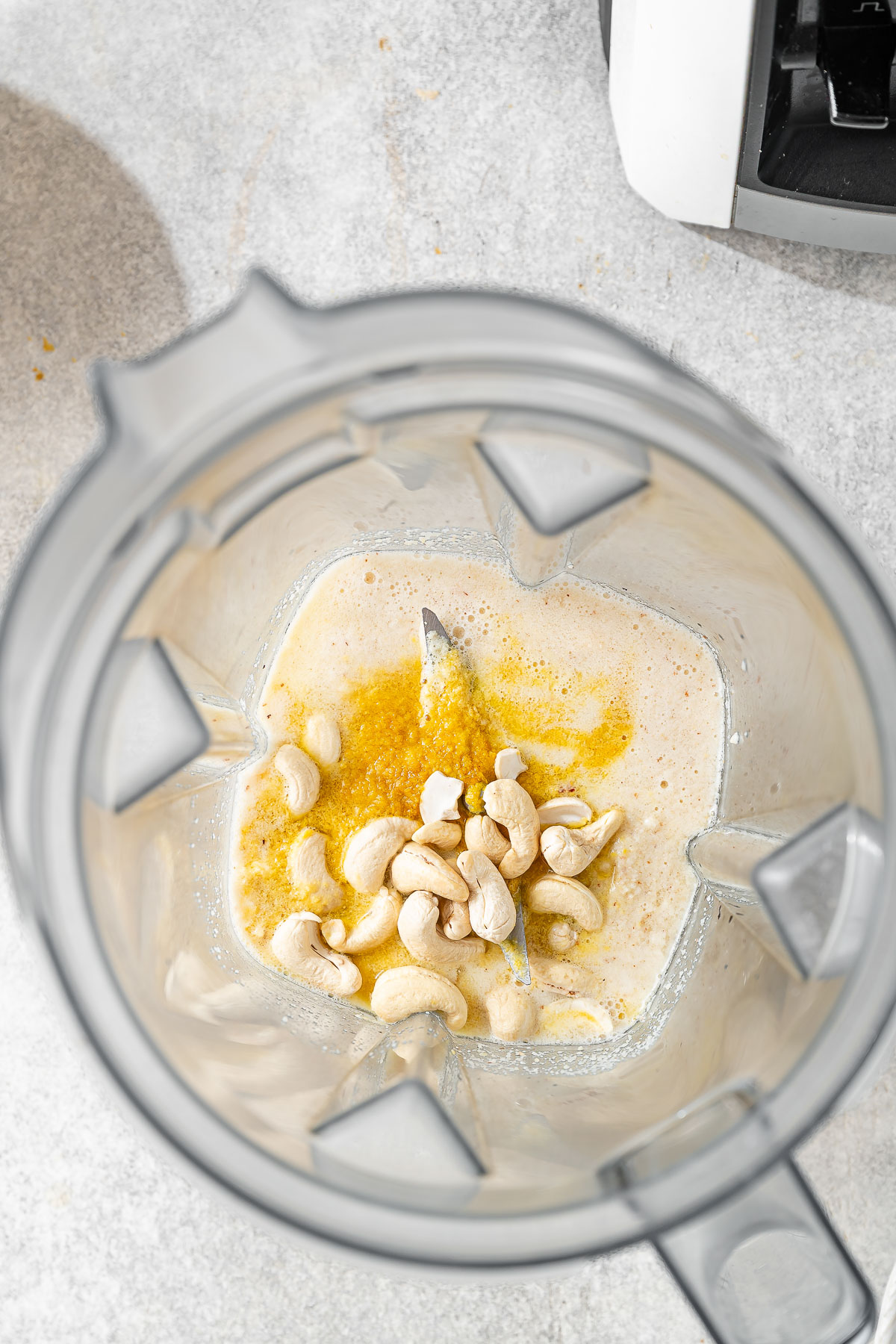 A high-speed blender filled with nuts, nutritional yeast, and liquid ingredients