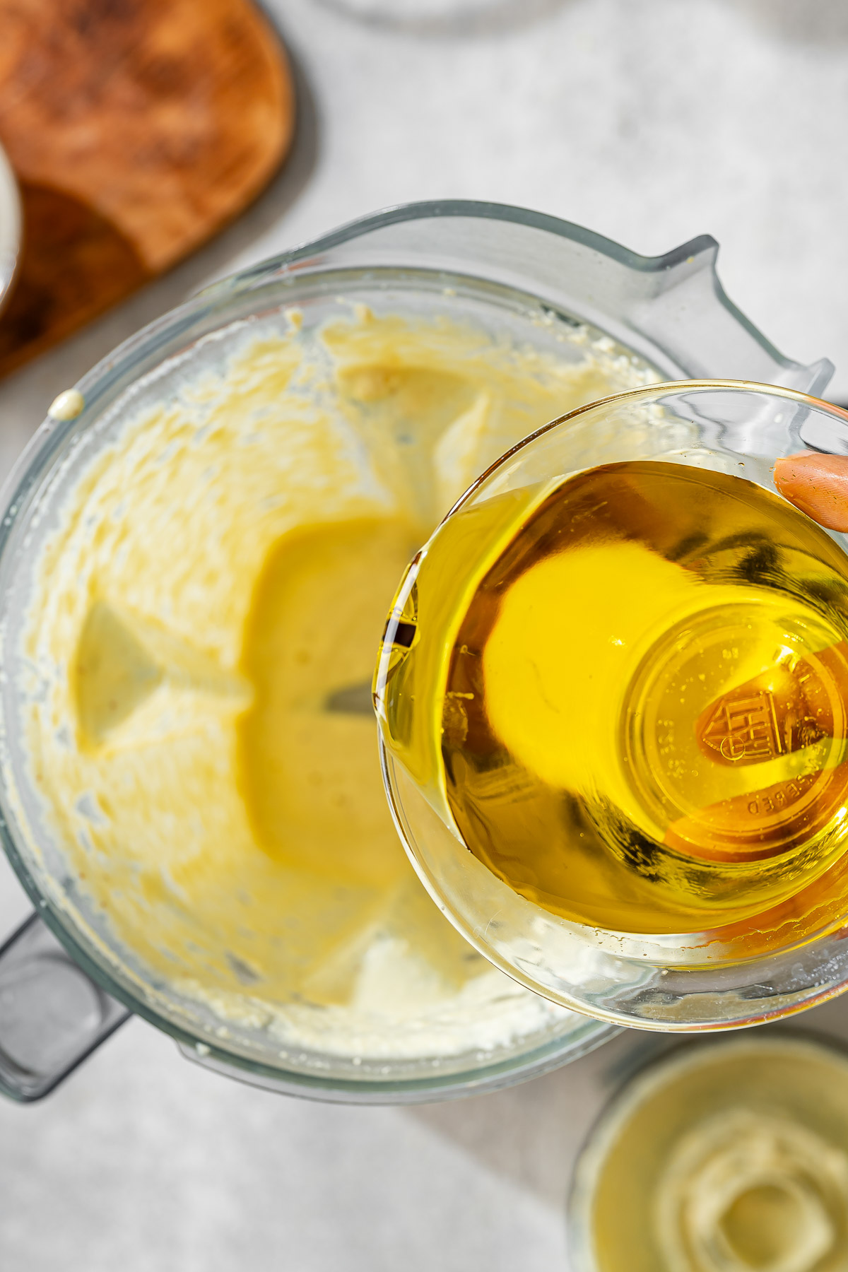 A person adding olive oil in the blended mixture