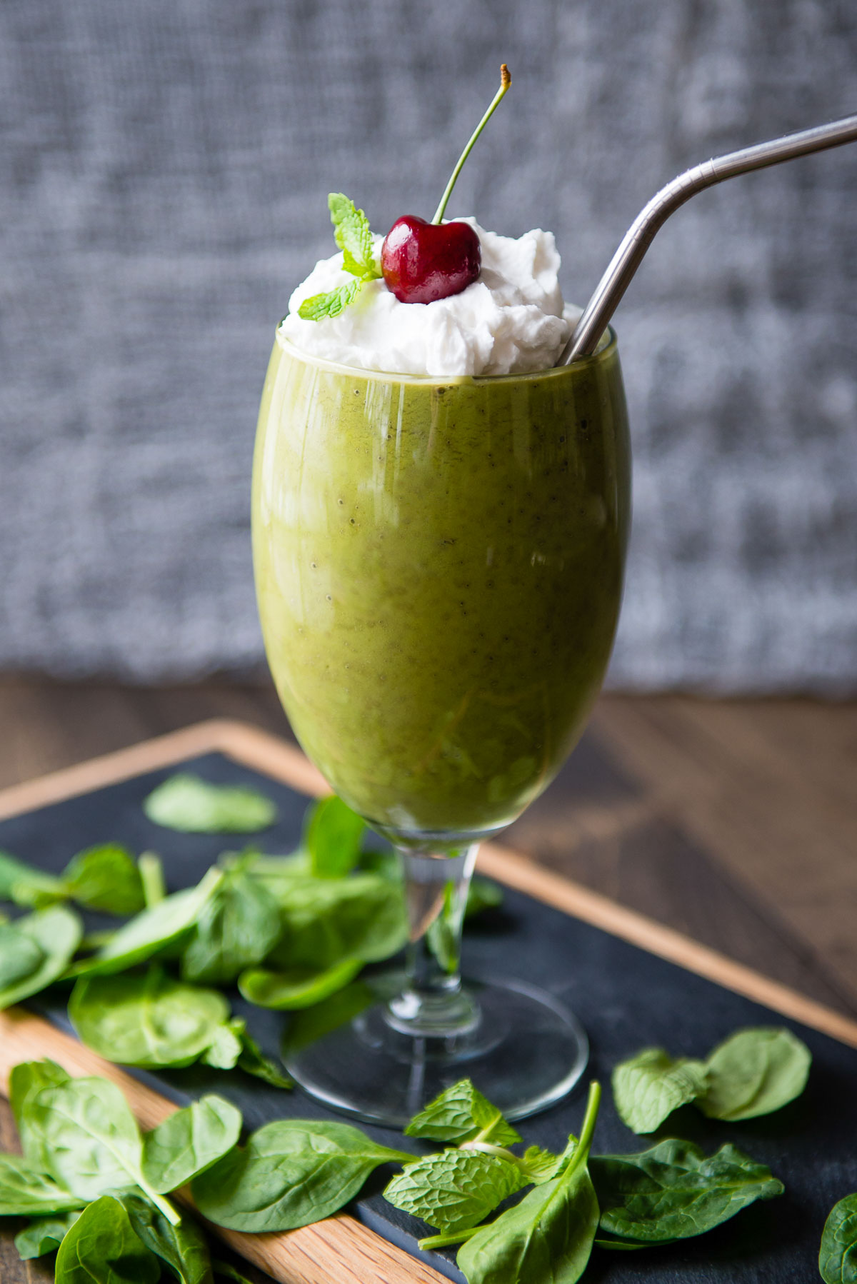 Side image of a vegan shamrock shake in a wine glass, garnished with coconut whipped cream, fresh mint, and a cherry.