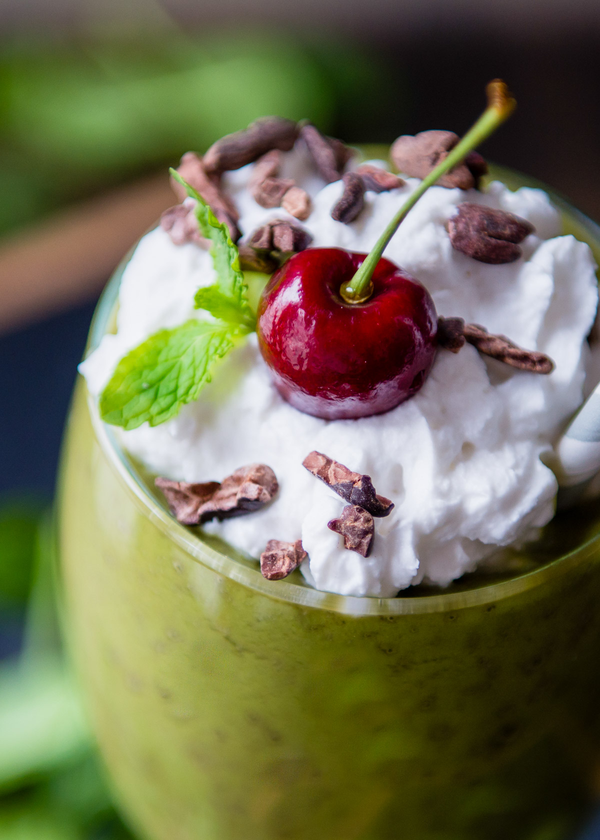 Close-up of a vegan Shamrock Shake topped with coconut whipped cream, cherry, and fresh mint.