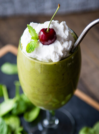 Vegan shamrock shake in a wine glass, topped with coconut whipped cream, fresh mint, and a cherry.