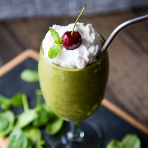 Vegan shamrock shake in a wine glass, topped with coconut whipped cream, fresh mint, and a cherry.