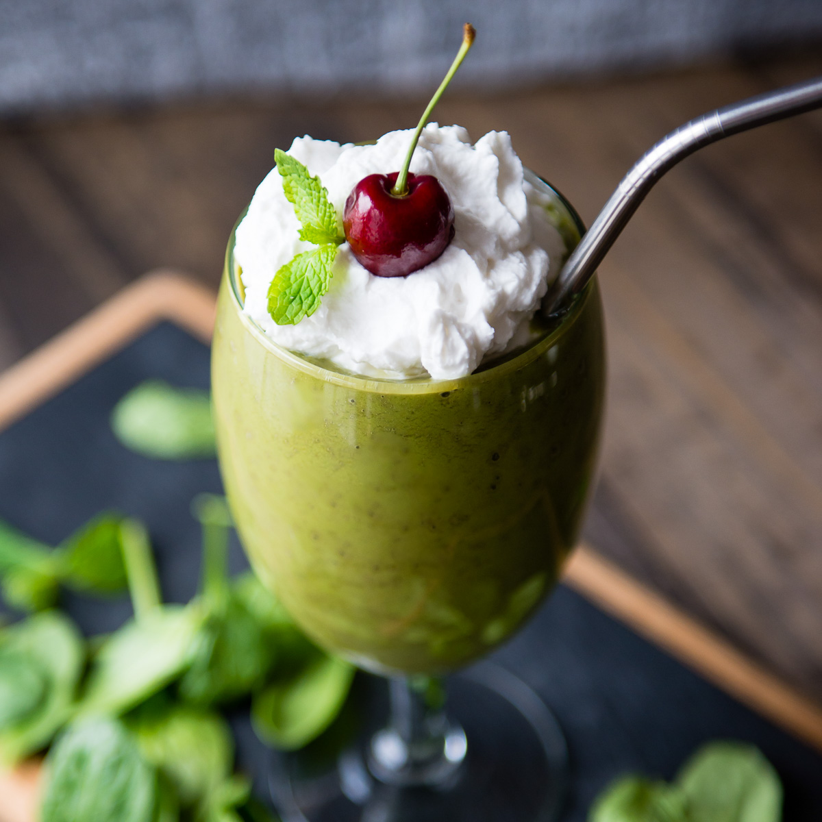Vegan shamrock shake in a wine glass, topped with coconut whipped cream, fresh mint, and a cherry.