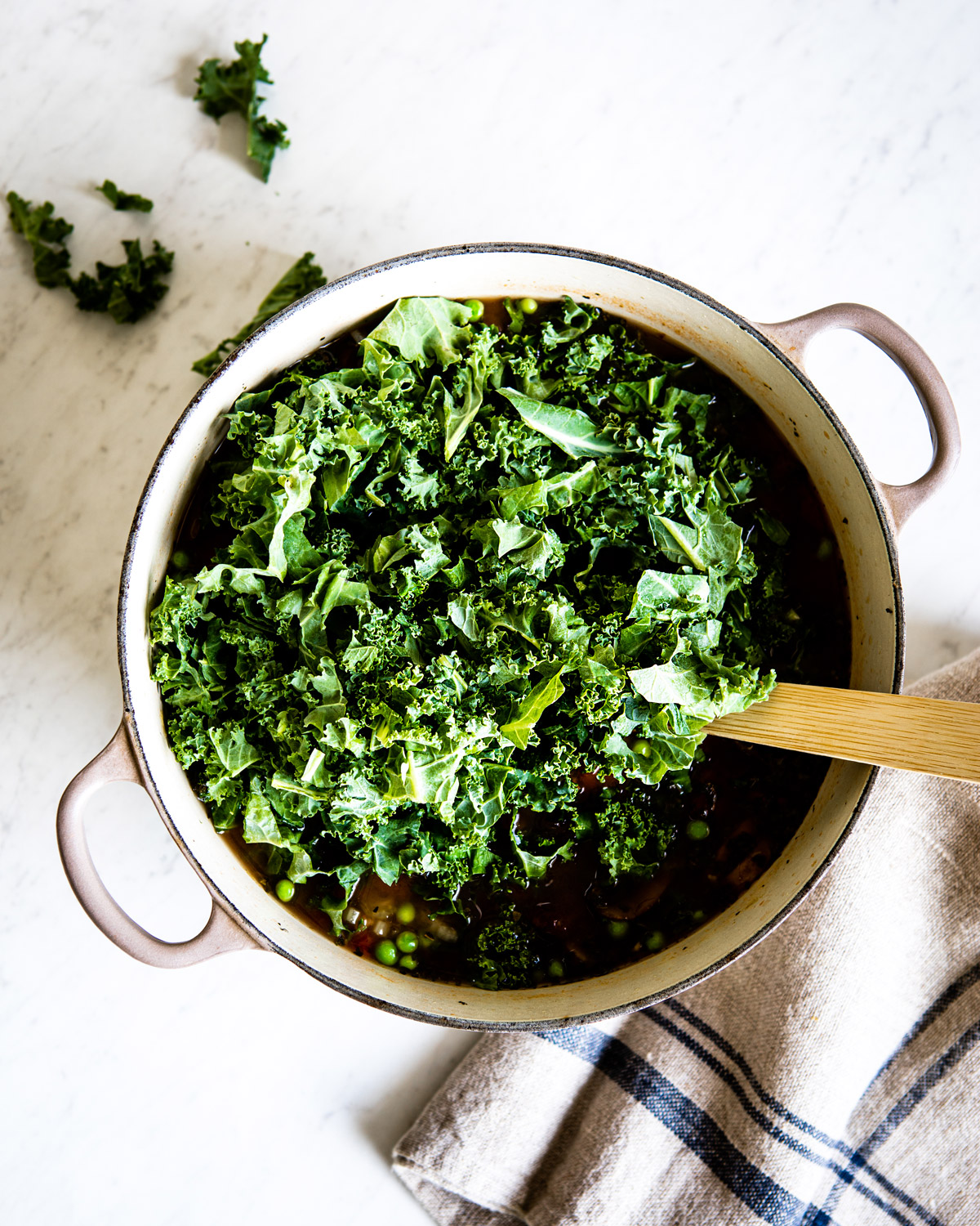 Chopped kale in a white enamel pot full of vegetable barley soup.