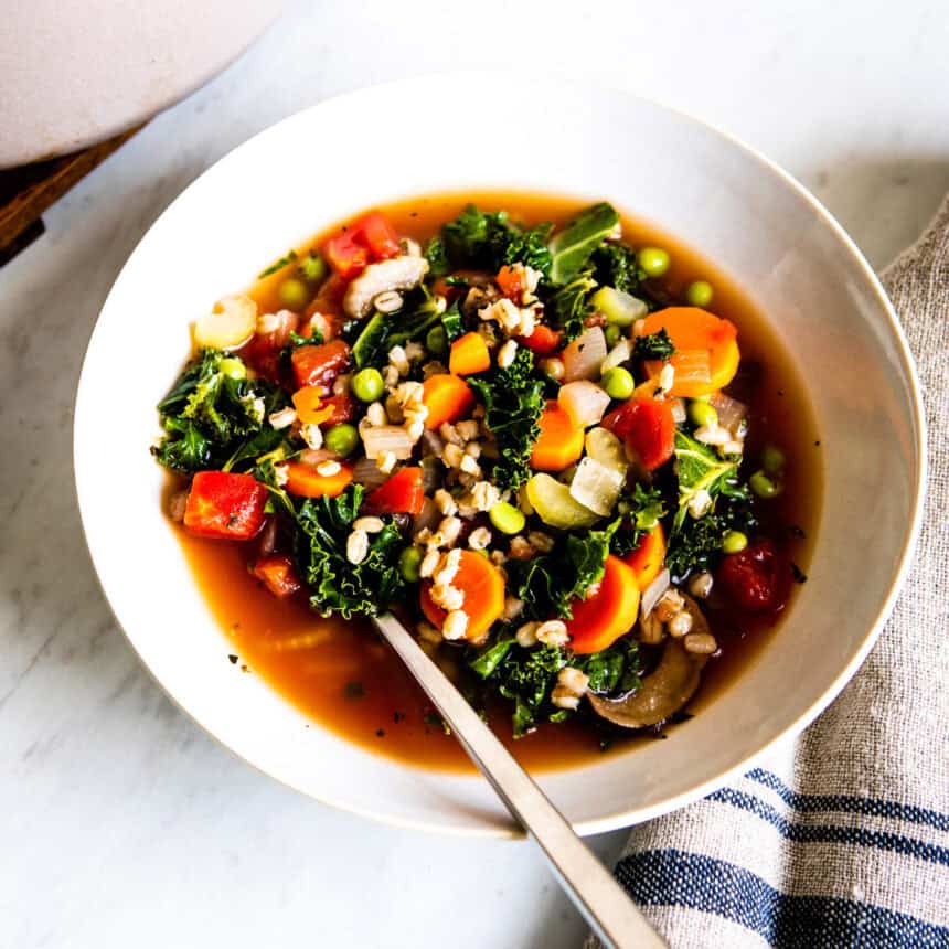 Spoon in a bowl of vegetable barley soup.
