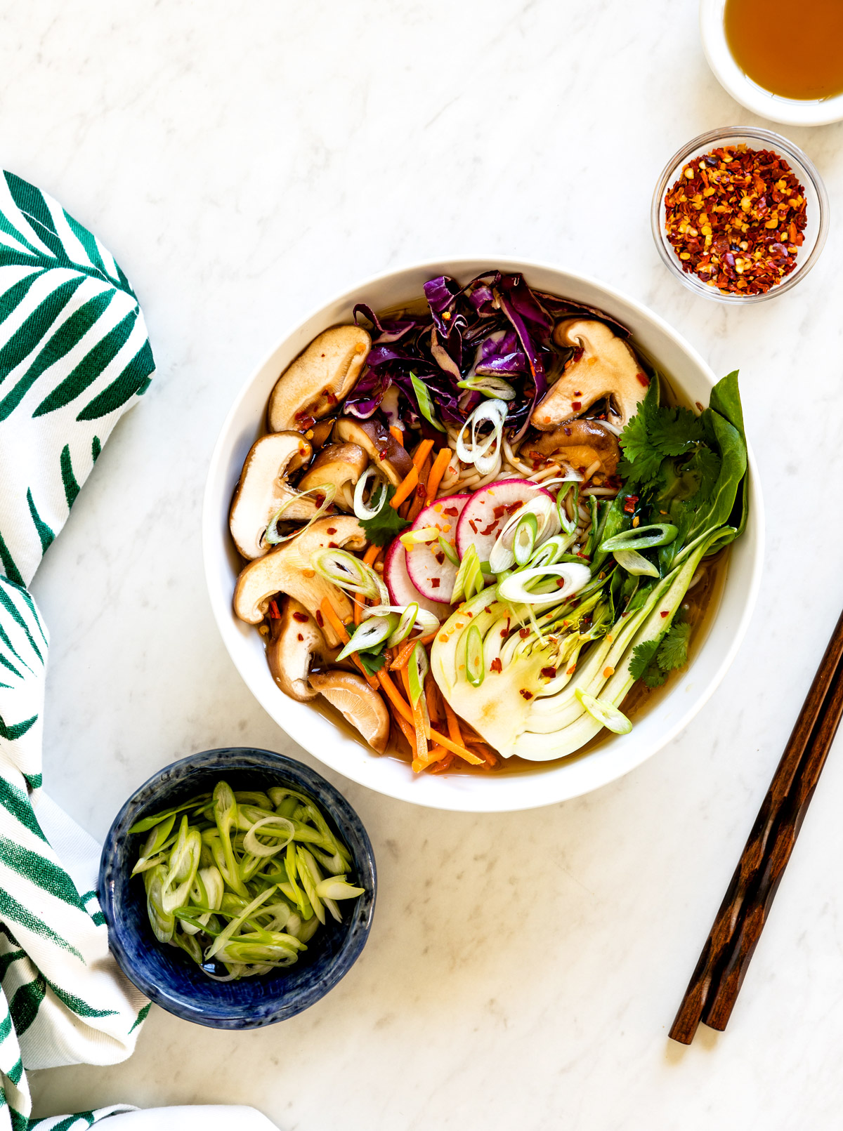 White shallow with bok choy, mushrooms and ramen noodles and chopsticks on the side.