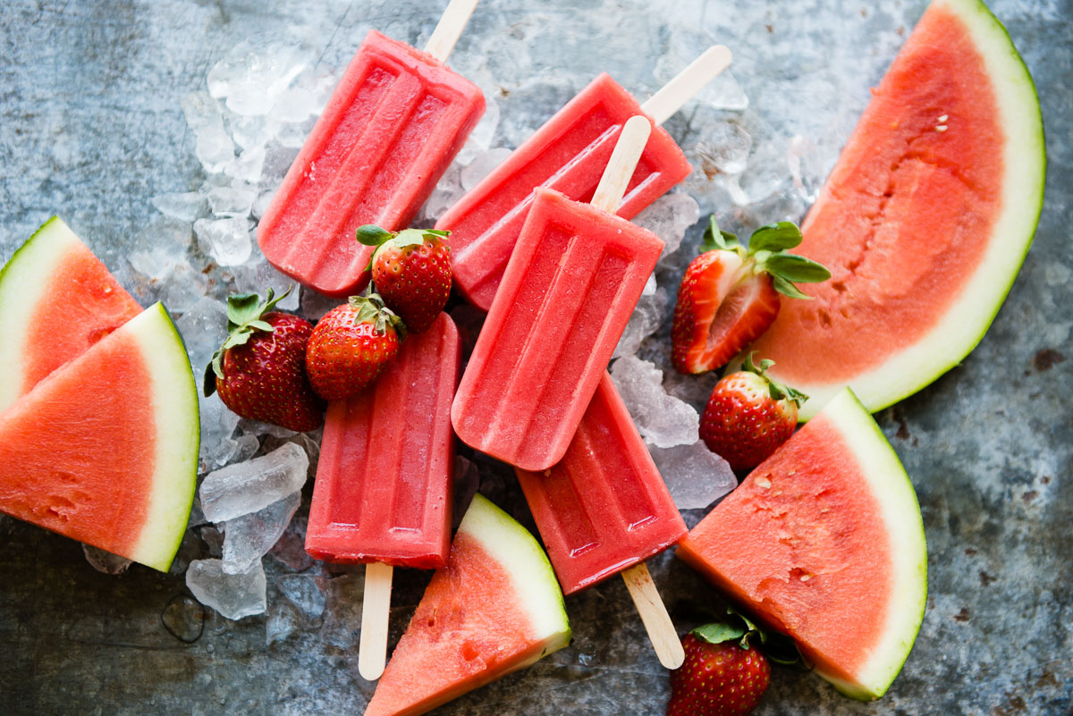 Watermelon popsicles laid on ice cubes and strawberries