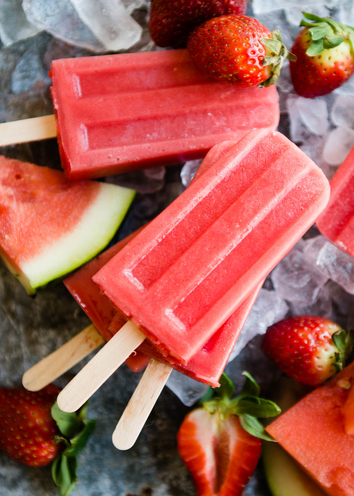 Homemade watermelon popsicles surrounded by watermelon slices and strawberries