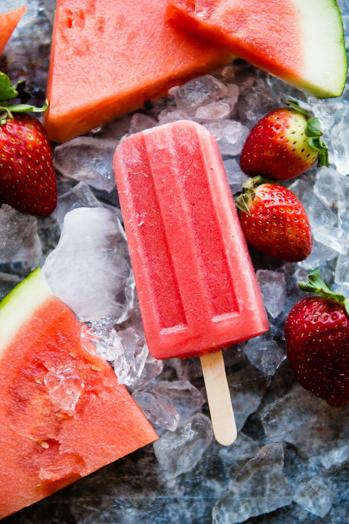 Fresh watermelon popsicles surrounded by watermelon pieces and strawberries