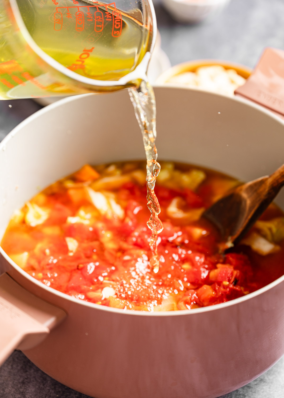 A person pouring vegetable stock in a large pot with veggies