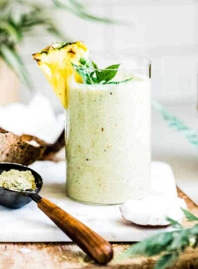 weight gain smoothie in glass with fresh pineapple and mint on top, next to a scoop of protein powder.