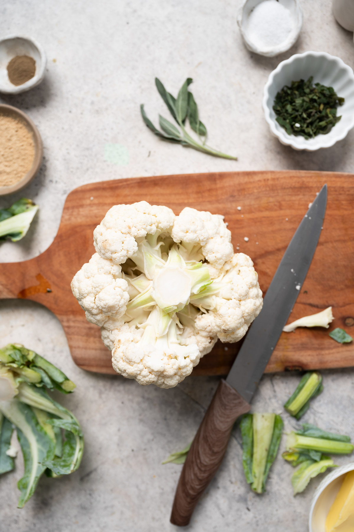 A head of cauliflower on a cutting board next to a knife, showing that all of the leaves have been trimmed off.