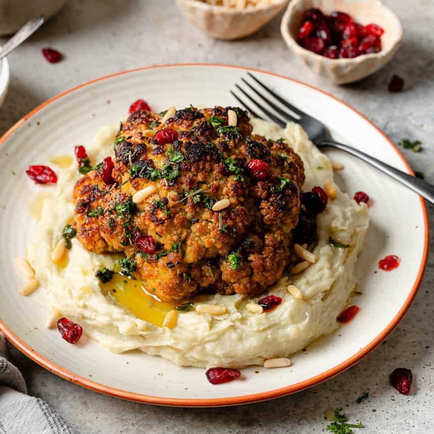 A whole roasted cauliflower head on a bed of mashed potatoes