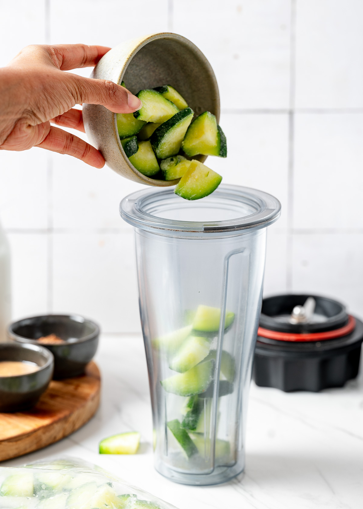 A person adding chopped zucchini in a blender