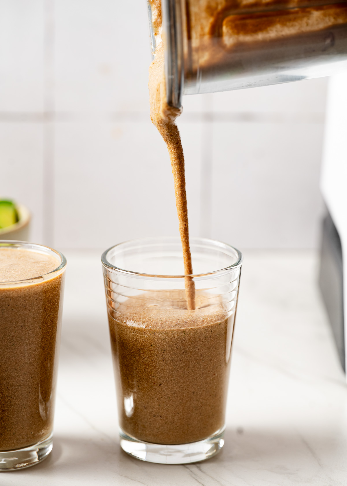 Pouring freshly blended zucchini smoothie into clear glasses