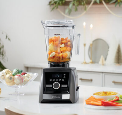 Gray blender with cut oranges and carrots in a white modern kitchen