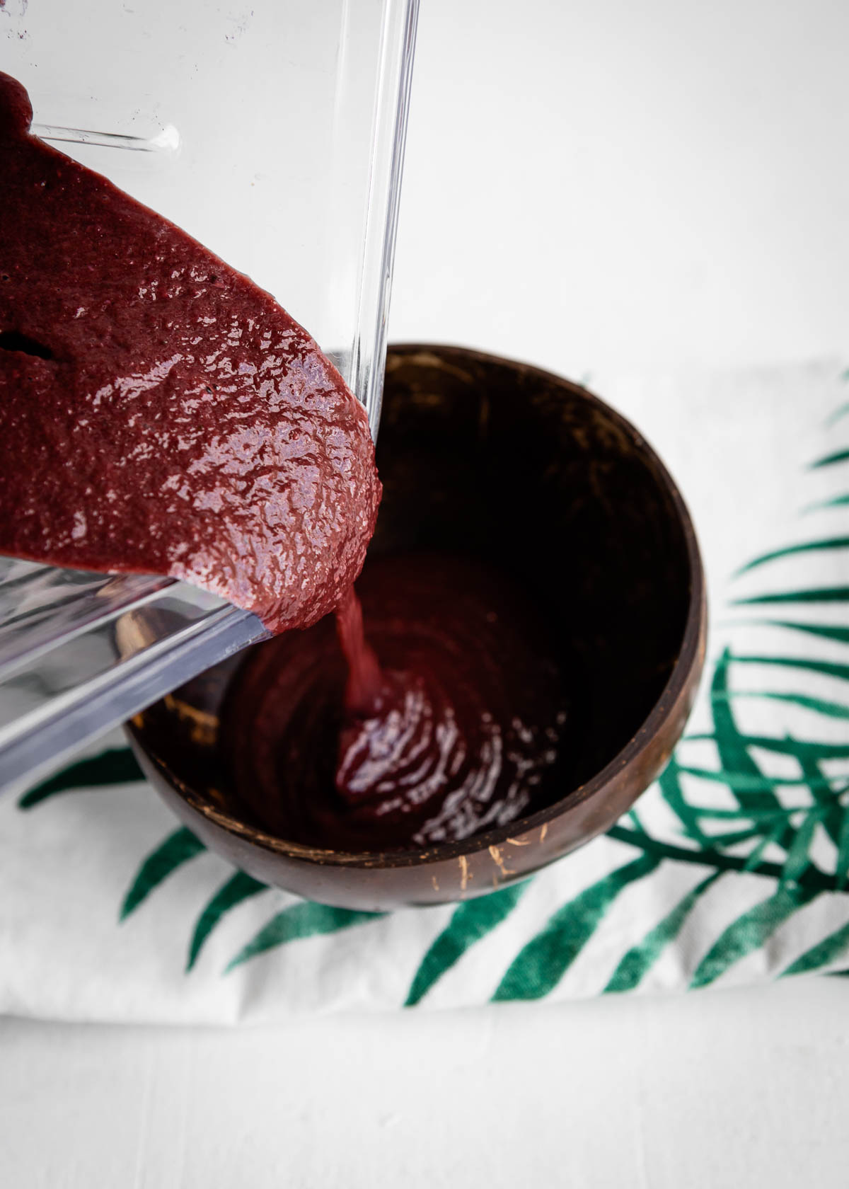 pouring acai smoothie bowl from a blender container into a coconut bowl.
