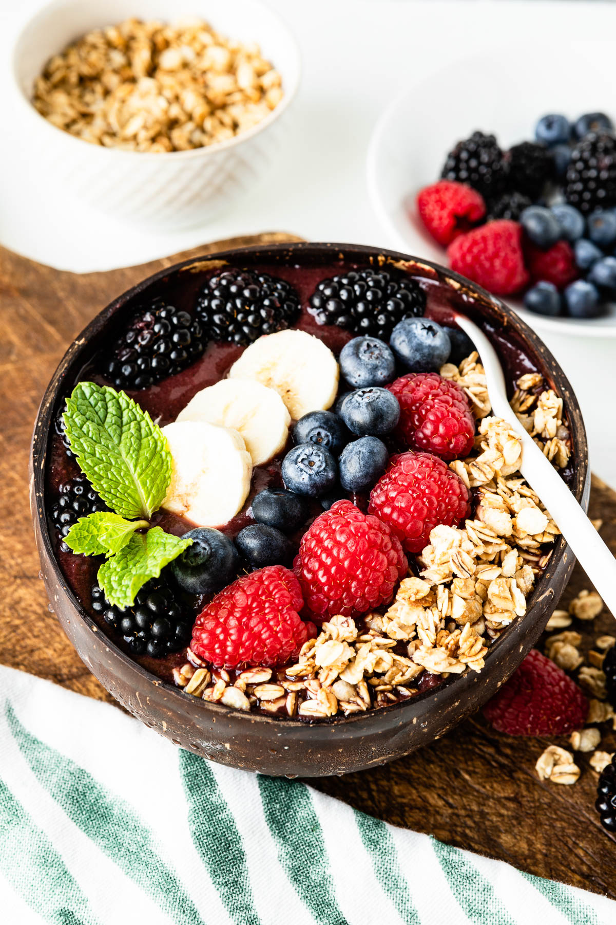 smoothie bowl topped with fresh berries, mint leaves and banana with a white spoon.