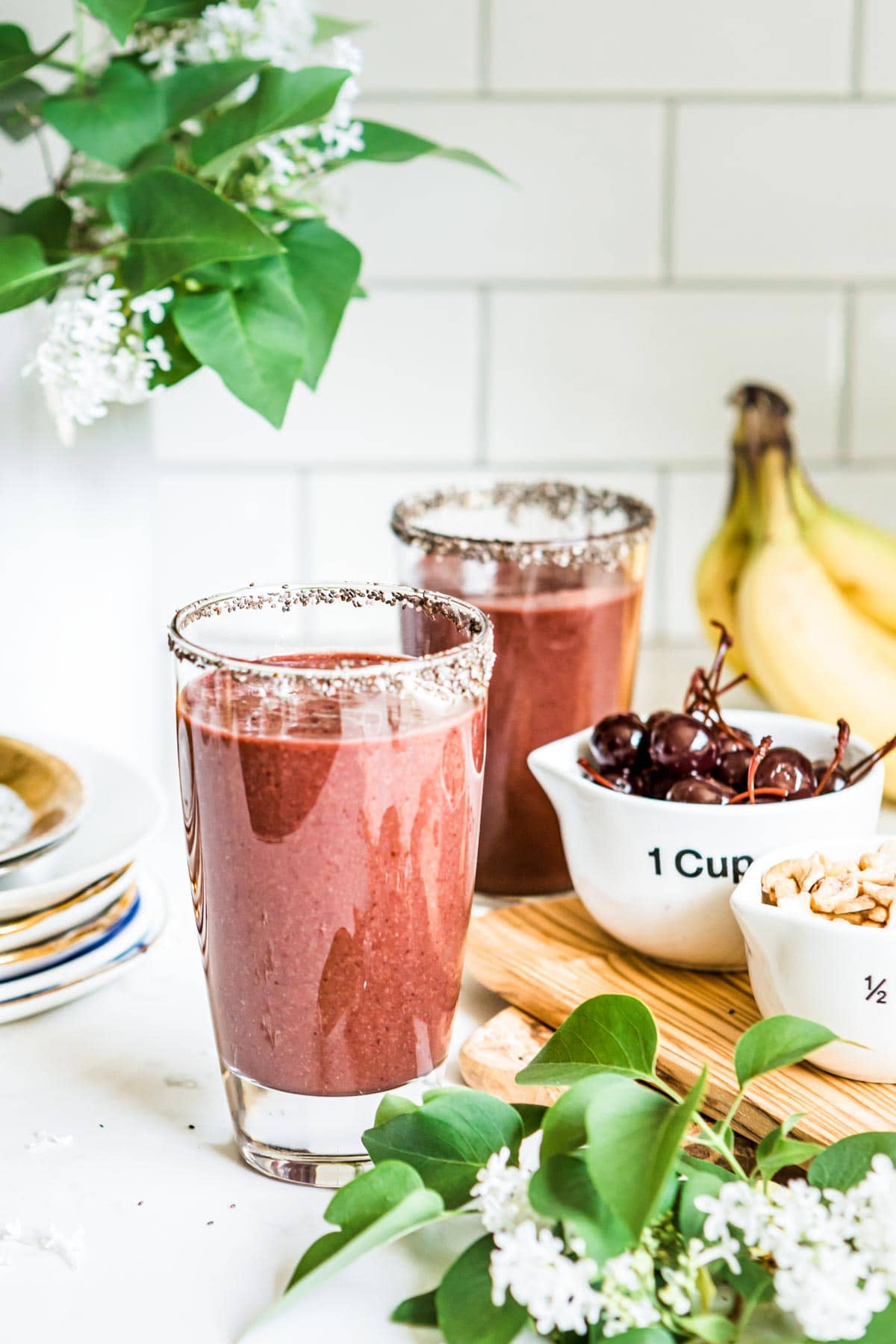 2 açai smoothies in glasses rimmed with chia seeds, next to bowls of cherries and cashews.