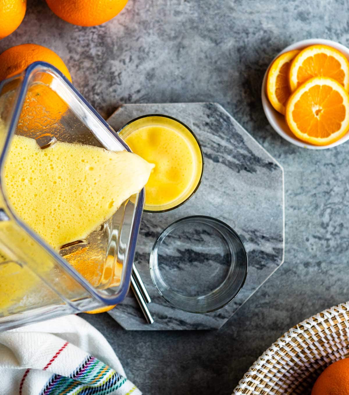 pouring orange beverage from a blender container into a glass on a marble slab