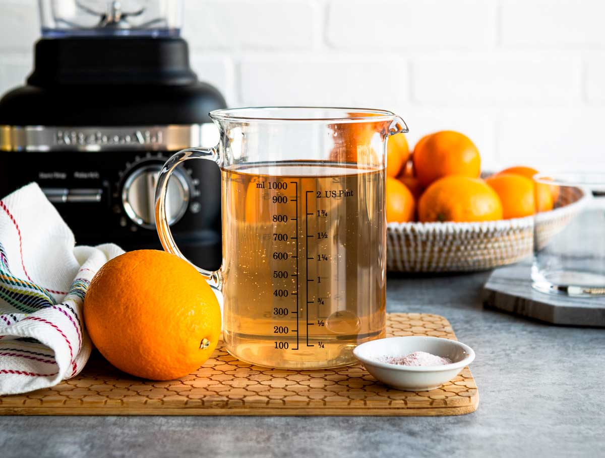 measuring glass with coconut water on a counter with whole orange and sea salt.