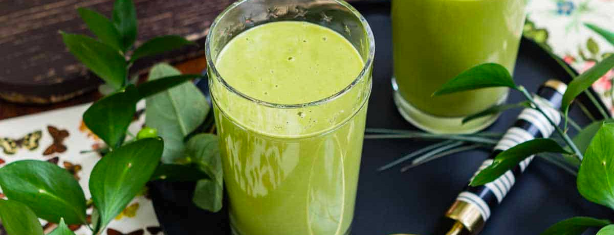 green smoothie in a glass with green leaves all around it
