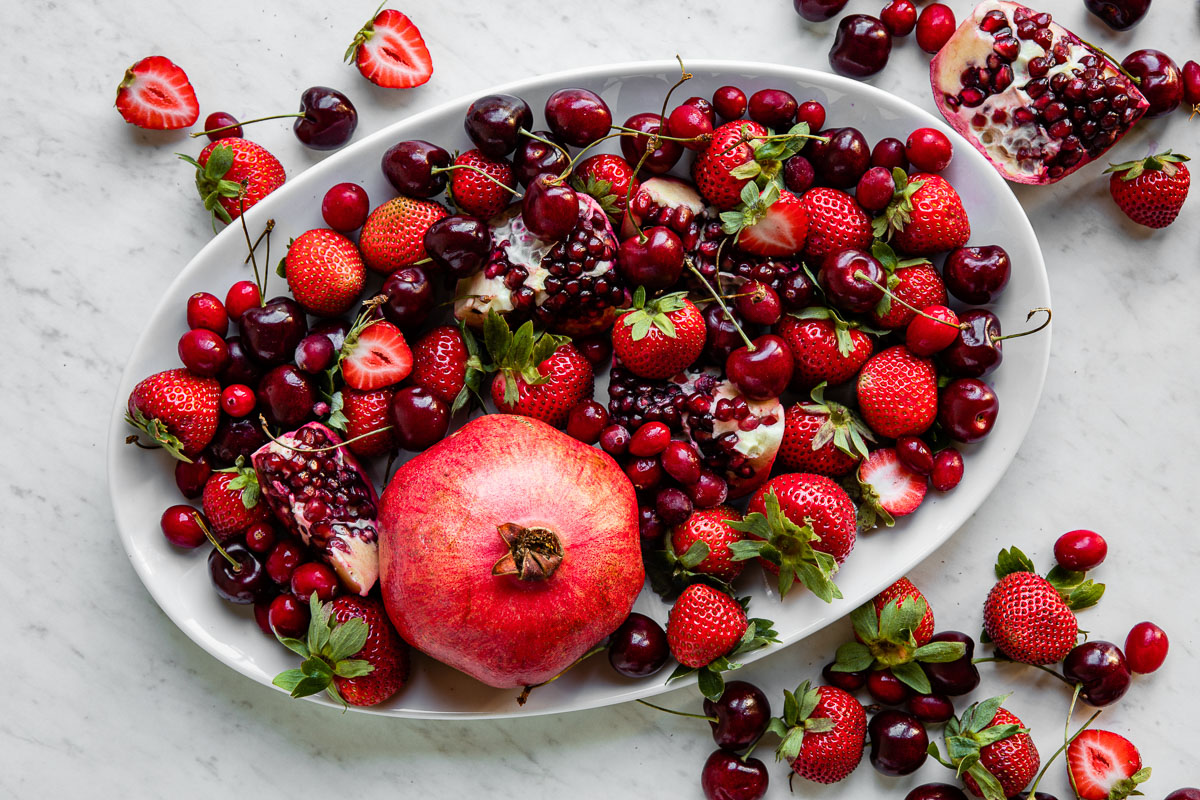 Large dish of vibrant red fruits, including strawberries, pomegranate seeds, and cherries.