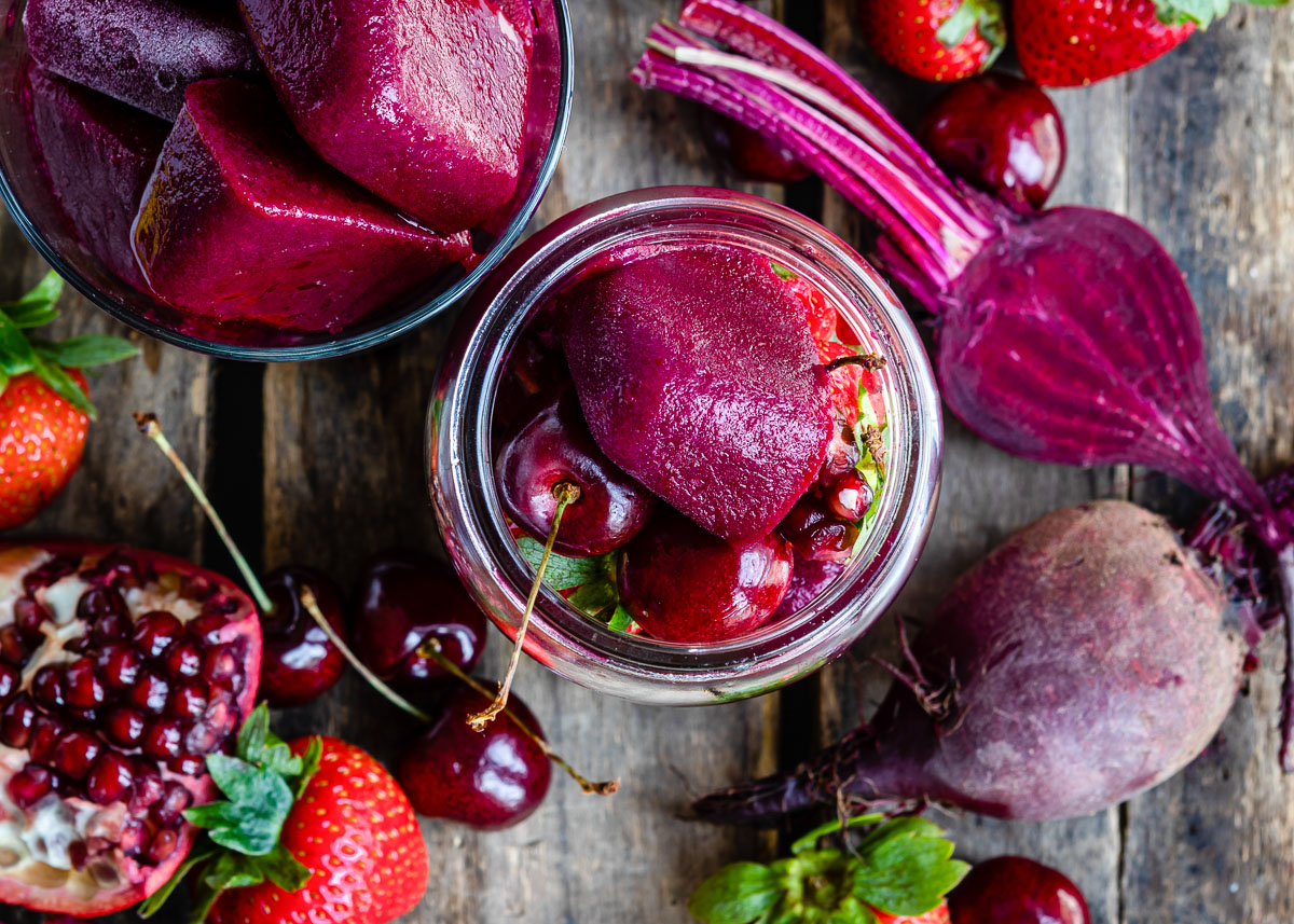 Overhead view of smoothie cubes in a Mason jar, surrounded by fresh, vibrant red and purple fruits and vegetables.