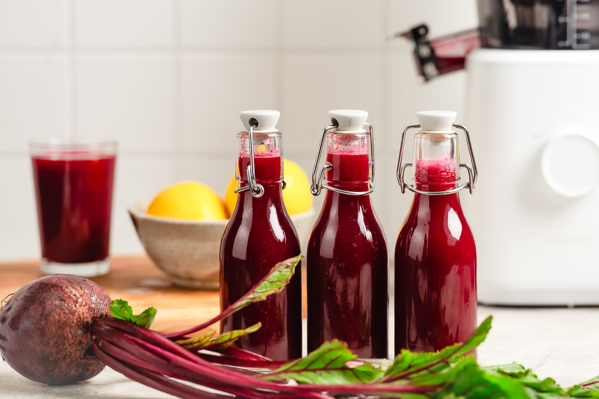 Three bottles of apple beet juice surrounded by fresh ingredients