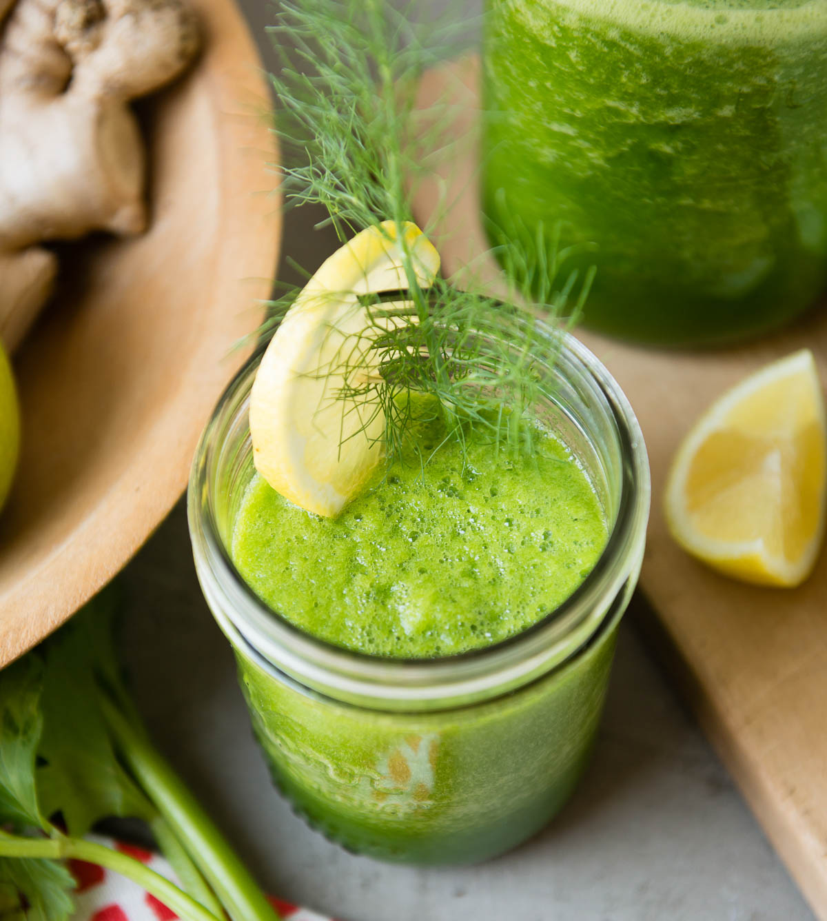 Frullato verde in un barattolo di vetro guarnito con uno spicchio di limone e foglie di finocchio.
