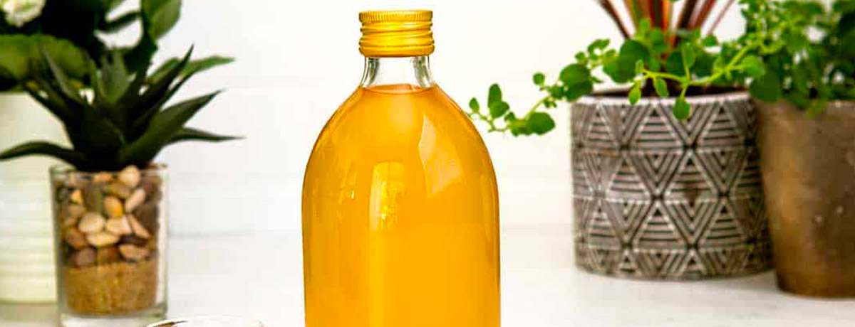 clear glass bottle of apple cider vinegar with plants in the background