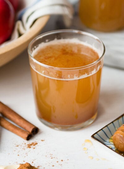 Apple cider vinegar drink in a small glass next to cinnamon sticks.