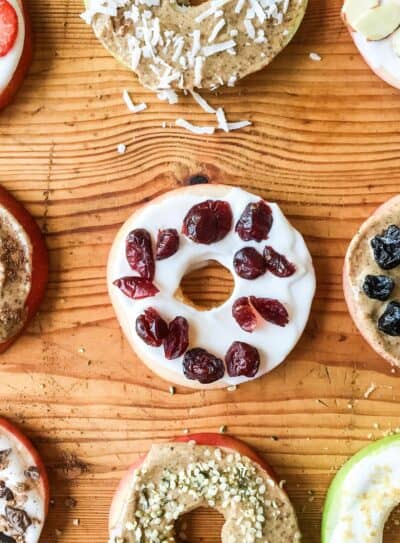 Colorful apple donuts with various toppings on a wooden surface.