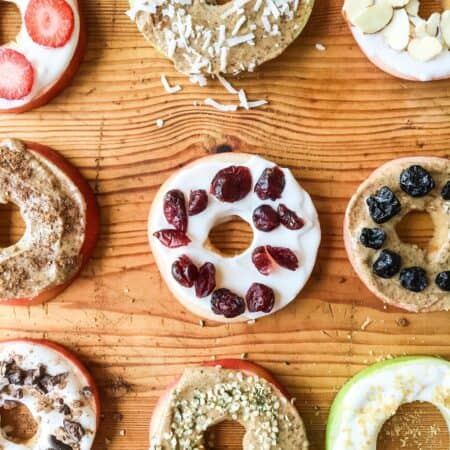 Colorful apple donuts with various toppings on a wooden surface.