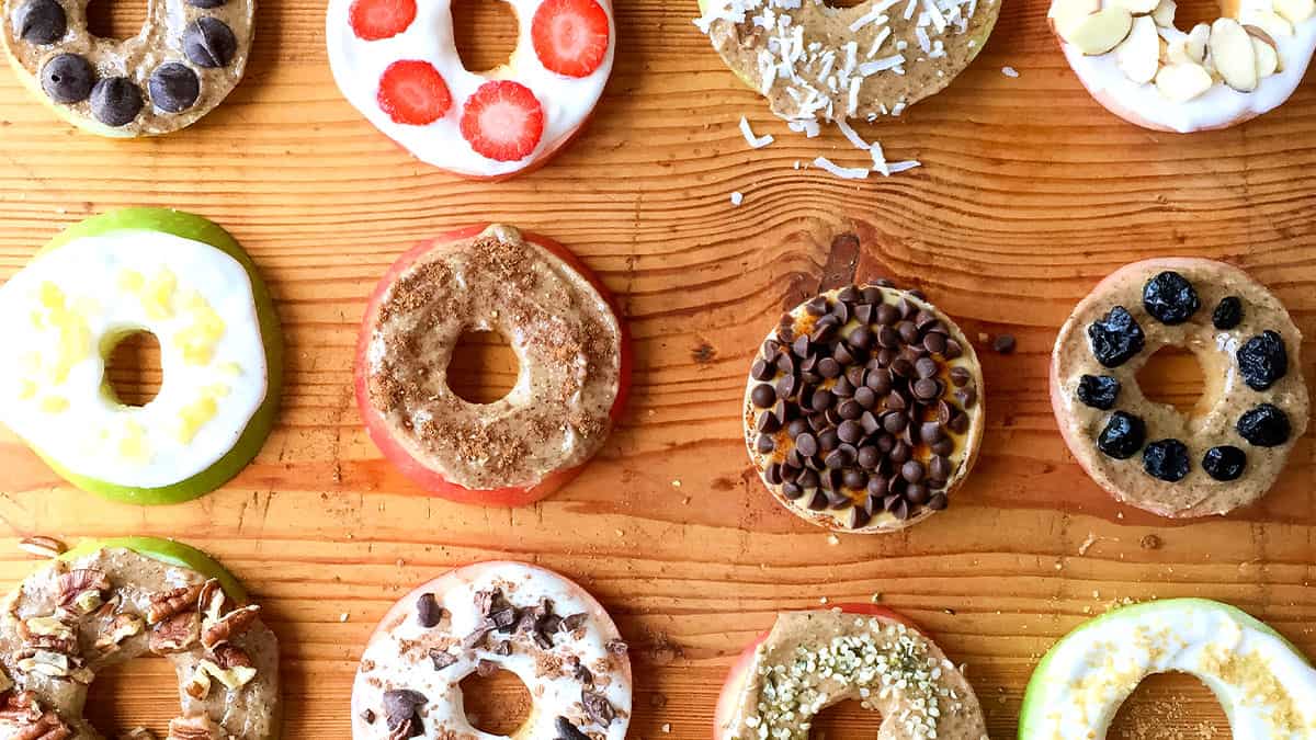 Colorful apple donuts with various toppings on a wooden surface.