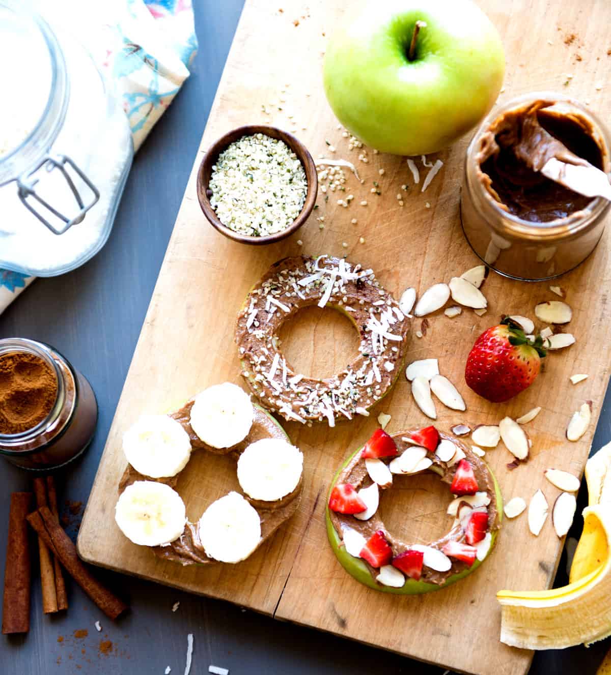 Healthy apple donuts with chocolate, strawberries, and almonds on a wooden board.