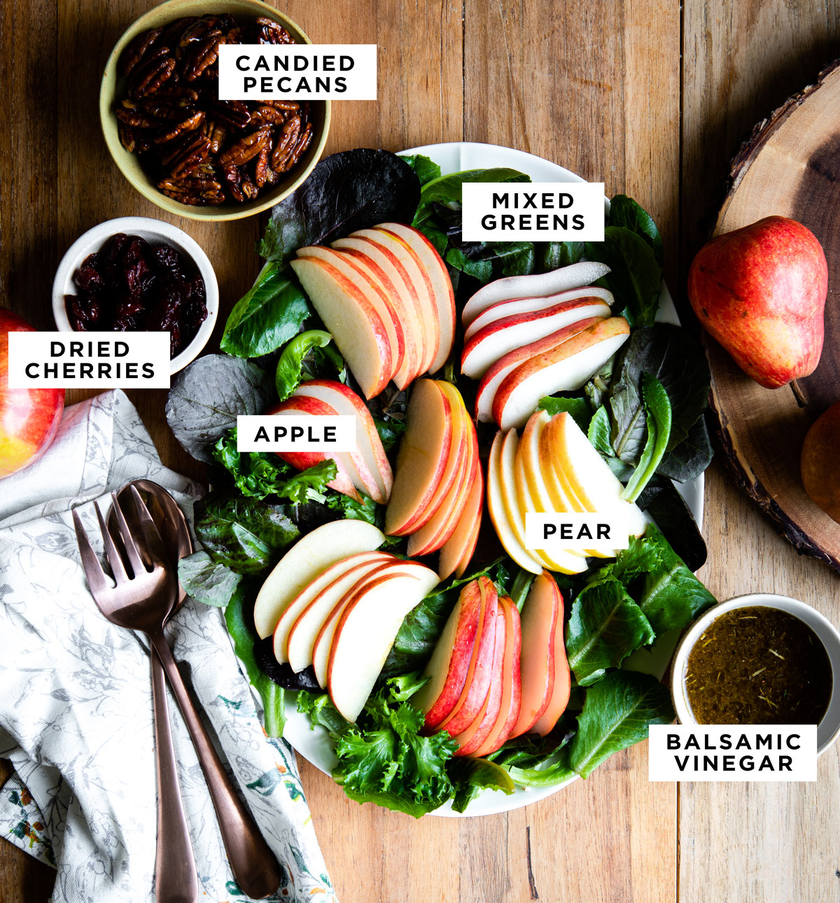 labeled ingredients for a green salad including candied pecans, mixed greens, dried cherries, apple, pear and balsamic vinegar.