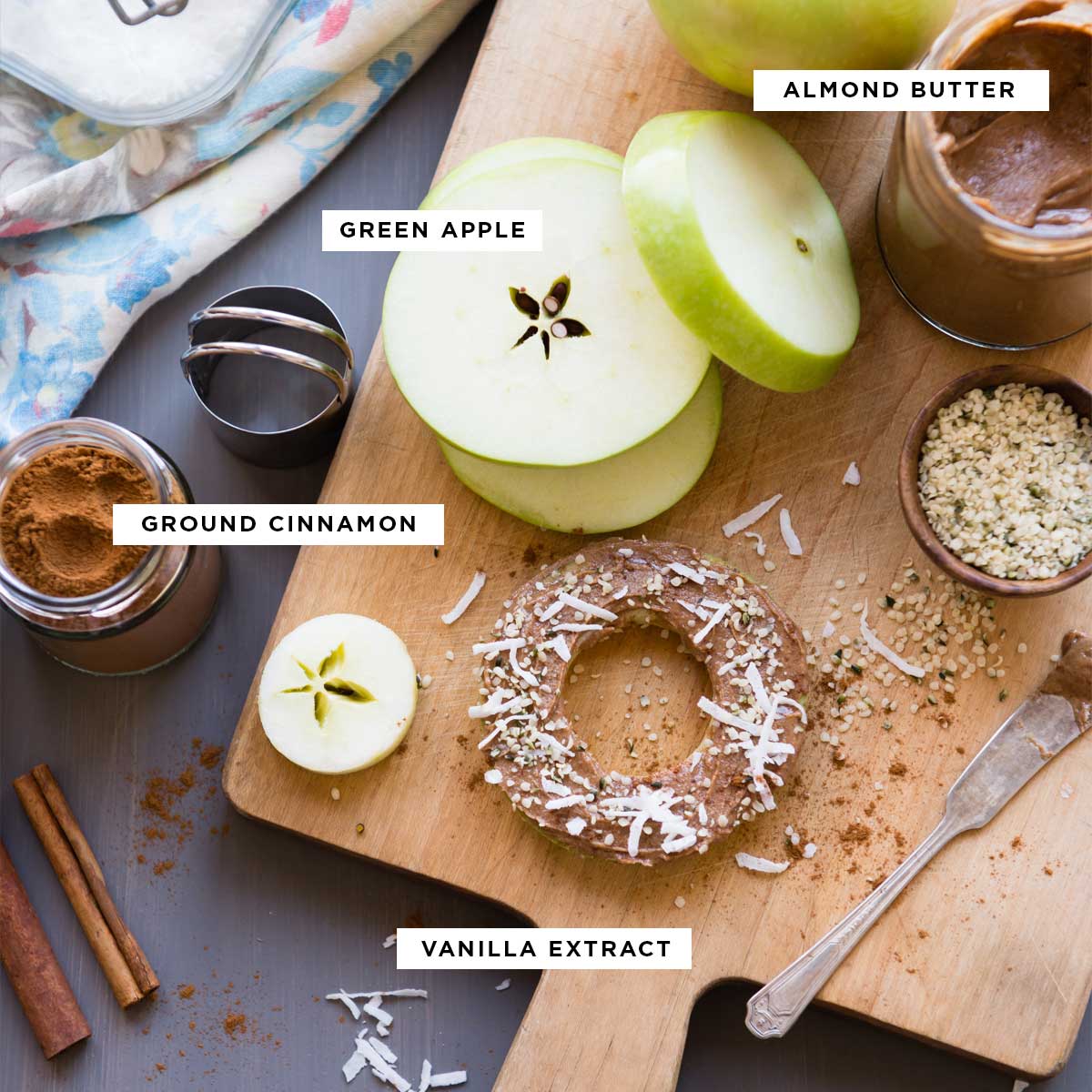 ingredients for apple snacks including almond butter, green apples, ground cinnamon and vanilla extract.