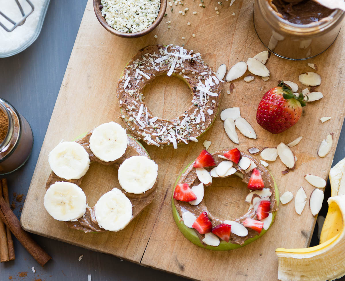 healthy apple snacks in the shape of donuts topped with nut butter and fresh fruit/nuts and seeds.