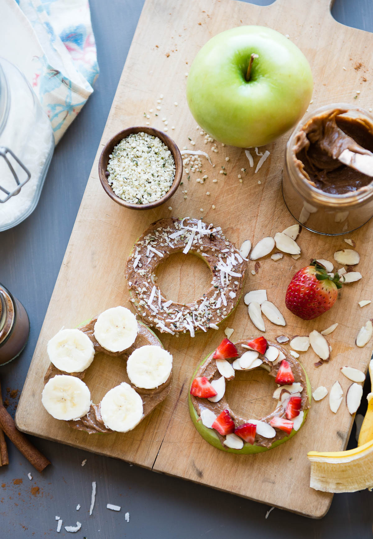 apples cut into donut shapes and topped with nut butter and a variety of toppings like coconut flakes, bananas and strawberries.