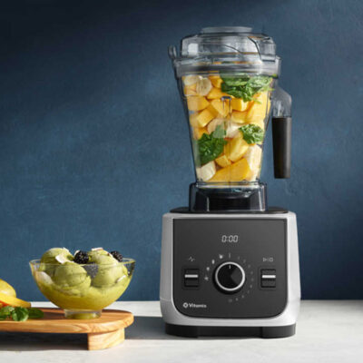 Vitamix blender loaded with spinach and mango on counter.