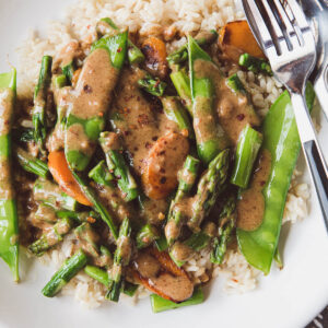 asparagus stir-fry with snow peas and carrots over a bed of rice and topped with almond butter sauce.